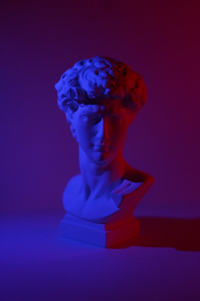 Bust of young male on plinth placed on white surface in dark studio in blue and red lights