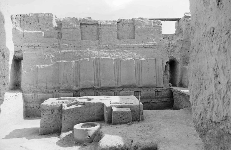 Photographie en noir et blanc des palais présargoniques superposés du site archéologique de Mari (Tell Hariri), datée de mai 1972. Vue intérieure montrant des murs en terre crue, des structures architecturales en briques crues, des niches et des ouvertures. Au premier plan, des vestiges de bases en pierre et une structure circulaire en terre cuite. Image issue des fouilles de la Mission archéologique franco-syrienne de Tell Hariri-Mari, archives de la MSH Mondes (réf. AP16280)